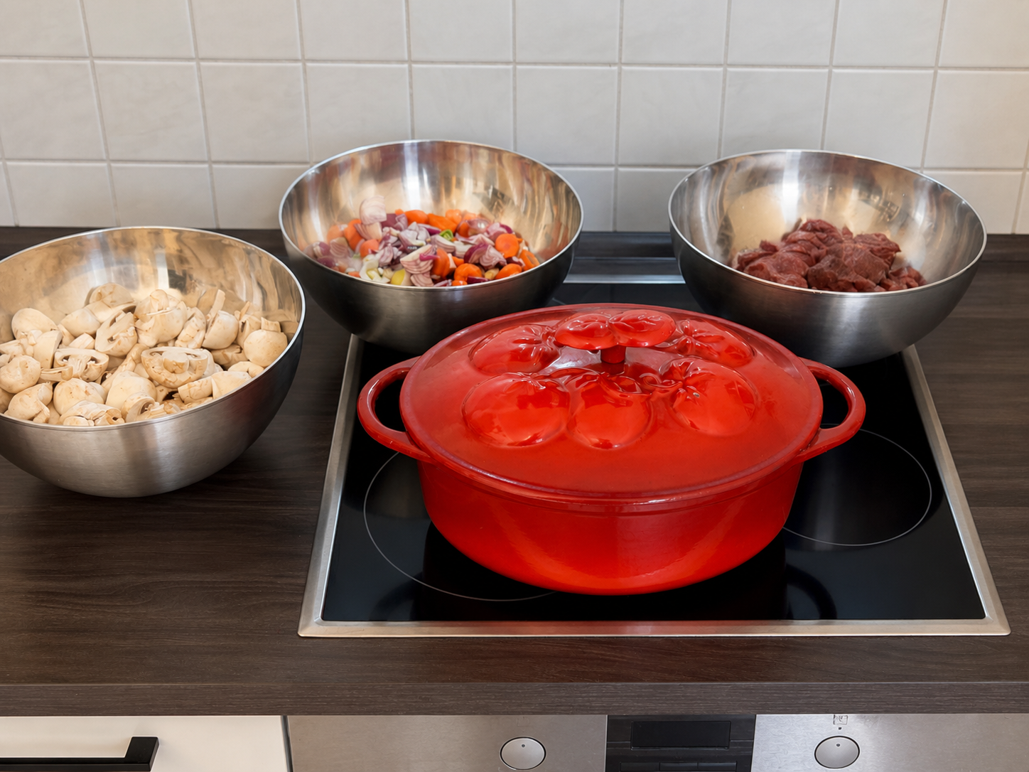 Vorbereitete Champignons, Karotten, Zwiebeln und Rindfleisch rund um einen roten Bräter