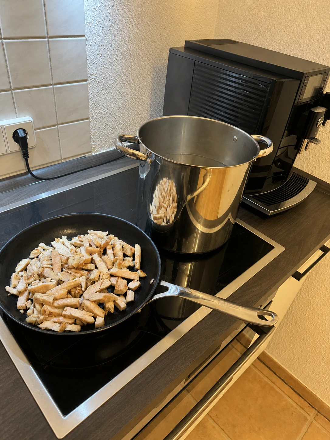 Gebratene Hähnchenstreifen in einer Pfanne neben dem Pastatopf