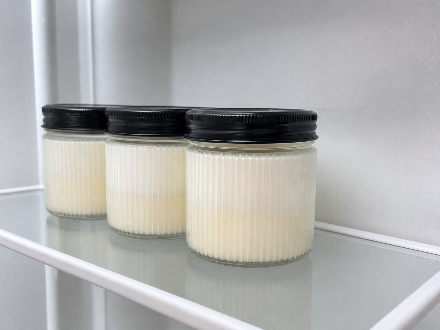 Abgedeckte Gläser mit Panna Cotta auf einer sauberen Kühlschrankablage
