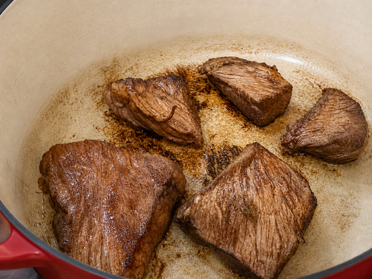Kräftig angebratene Rindfleischstücke mit braunem Bratensatz im gusseisernen Bräter