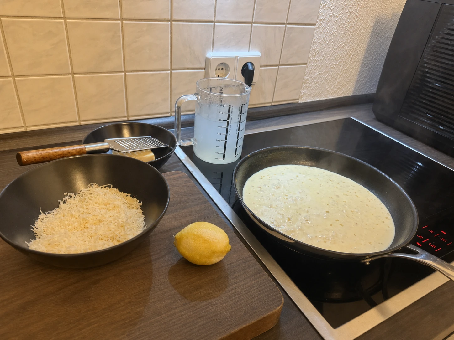Cremige Sauce in der Pfanne mit geriebenem Parmesan, Zitrone und Nudelwasser